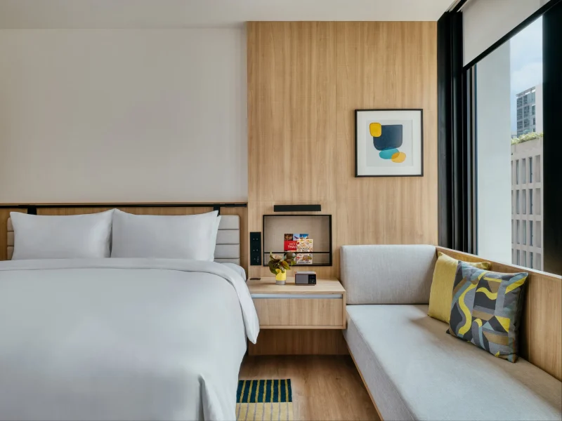 voco Surawong king room with wood paneling, window seat, and abstract wall art