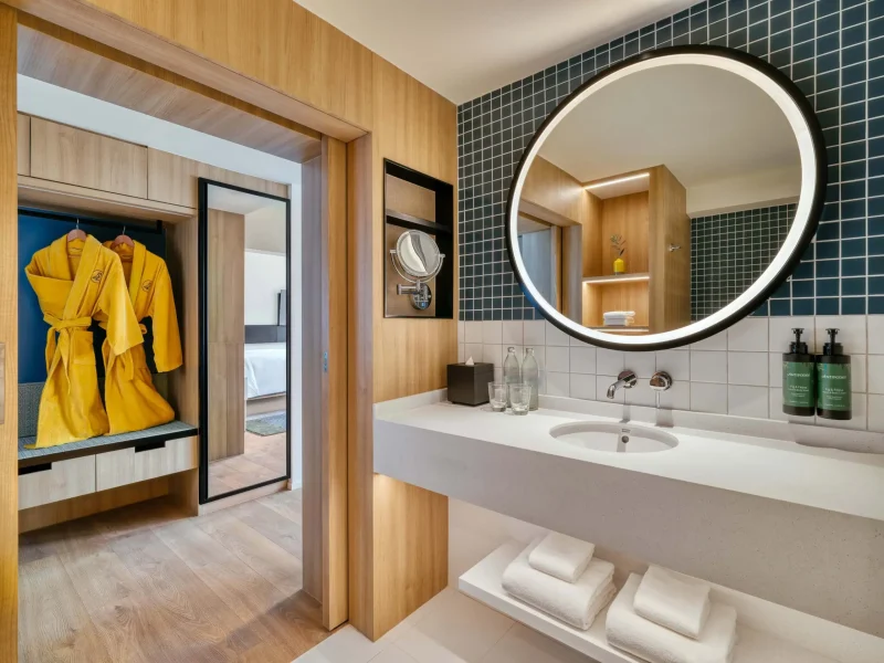 voco Surawong bathroom with round mirror, dark mosaic tile, and yellow robes in adjoining closet