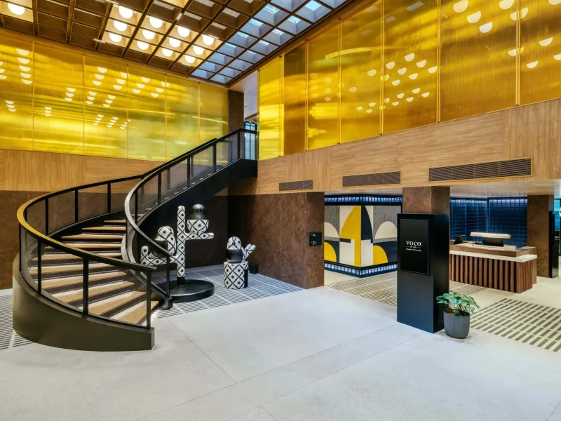 Spiral staircase and reception desk in the voco Surawong lobby, with gold screen wall and patterned bird sculptures
