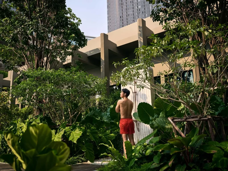 Man using an outdoor garden shower at voco Surawong, surrounded by lush tropical greenery in Bangkok