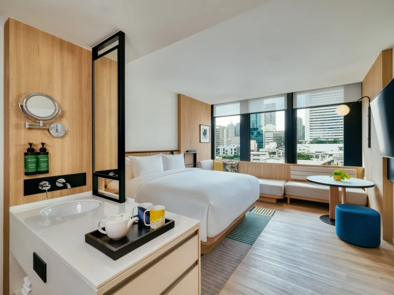 voco Surawong guest room with open bathroom vanity, tea set, and Bangkok skyline view