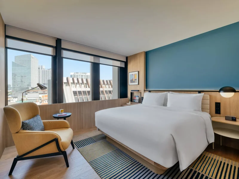 voco Surawong suite with teal accent wall, armchair, and city skyline view