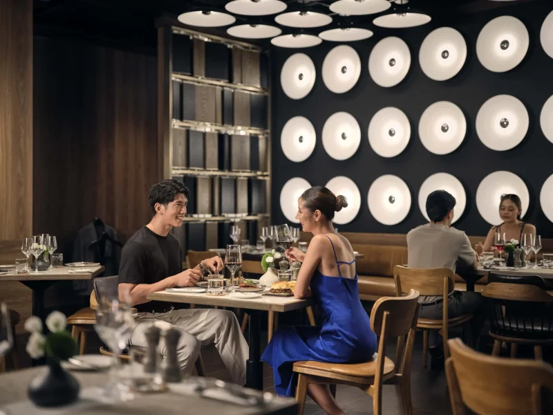 Couple enjoying dinner and wine at voco Surawong's restaurant in Bangkok, with distinctive circular wall lighting
