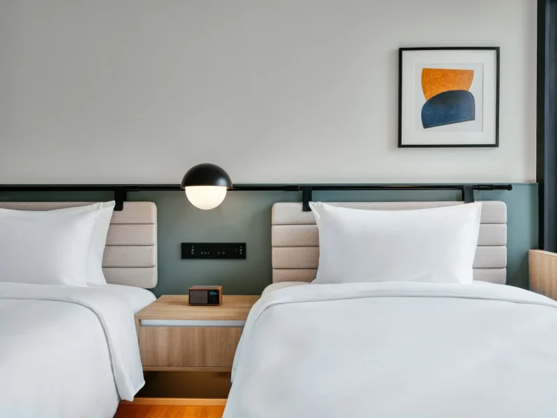 Twin beds with shared nightstand and globe wall light in a voco Surawong guest room